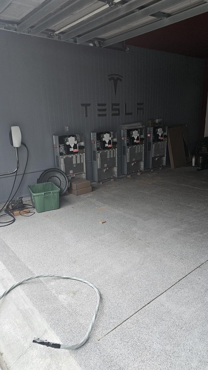 Bank of four Tesla Powerwall battery units installed against a wall with the Tesla logo